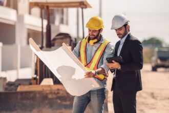 Profissionais da construção analisando planta da obra no canteiro, representando o processo de orçamento de obra passo a passo, com planejamento e controle de custos.