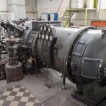 Equipamento industrial de grande porte com cilindro metálico, válvulas e painel de manômetros instalado em ambiente fabril para controle de pressão e processos técnicos.