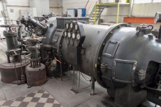 Equipamento industrial de grande porte com cilindro metálico, válvulas e painel de manômetros instalado em ambiente fabril para controle de pressão e processos técnicos.