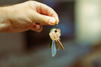 Mão segurando um molho de chaves com chaveiro, simbolizando entrega de imóvel alugado e início de contrato de locação.
