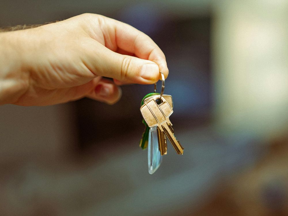 Mão segurando um molho de chaves com chaveiro, simbolizando entrega de imóvel alugado e início de contrato de locação.