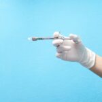 Mão com luva segurando seringa com anestésico em fundo azul, representando o que é anestesia local.