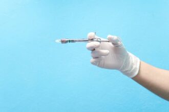 Mão com luva segurando seringa com anestésico em fundo azul, representando o que é anestesia local.