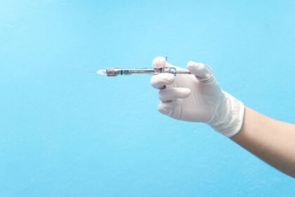 Mão com luva segurando seringa com anestésico em fundo azul, representando o que é anestesia local.